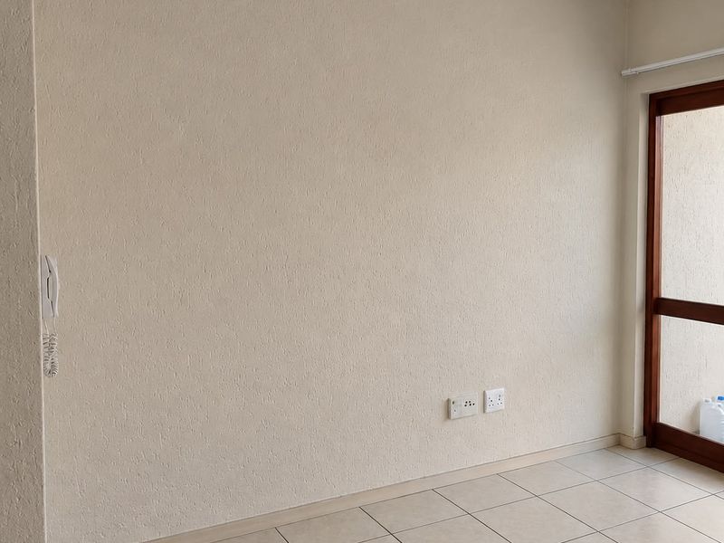 A bright, empty living area featuring neutral tiled flooring, a glass panel door, and an integrated intercom system.