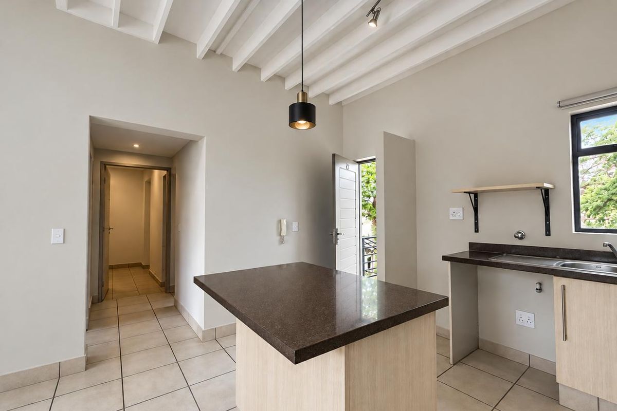 A bright, modern kitchen featuring exposed ceiling beams, a central island with stone countertops, tiled flooring, and direct access to an outdoor area.