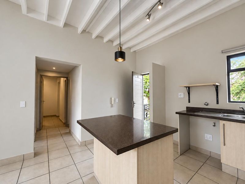 A bright, modern kitchen featuring exposed ceiling beams, a central island with stone countertops, tiled flooring, and direct access to an outdoor area.