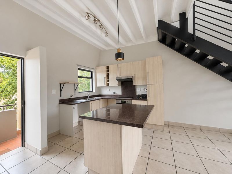Open-plan kitchen featuring light wood cabinetry, dark stone countertops, integrated appliances, and a modern metal staircase leading to an upper level.