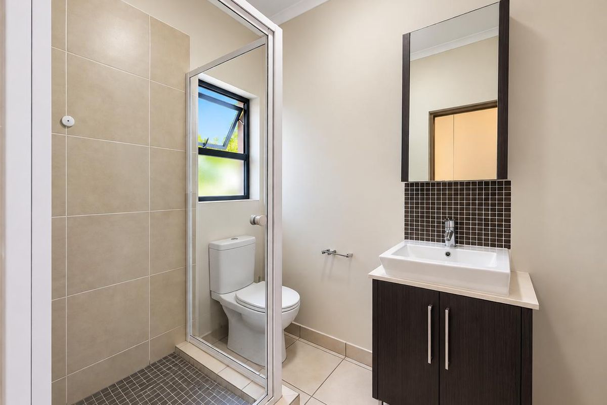 A clean and modern bathroom featuring a glass-enclosed shower, a contemporary vanity with a basin, and neutral floor and wall tiling.