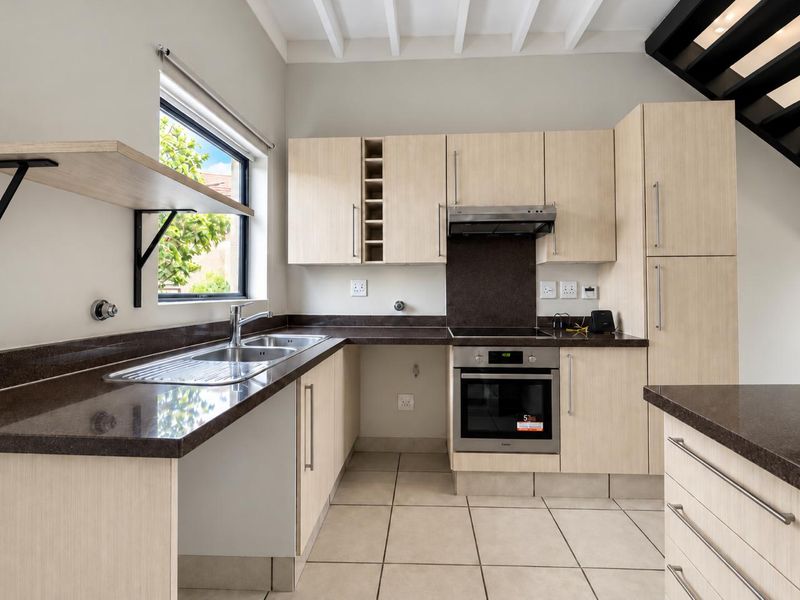 Modern kitchen featuring light wood cabinetry, dark stone countertops, integrated stainless steel appliances, and tiled flooring under exposed ceiling beams.