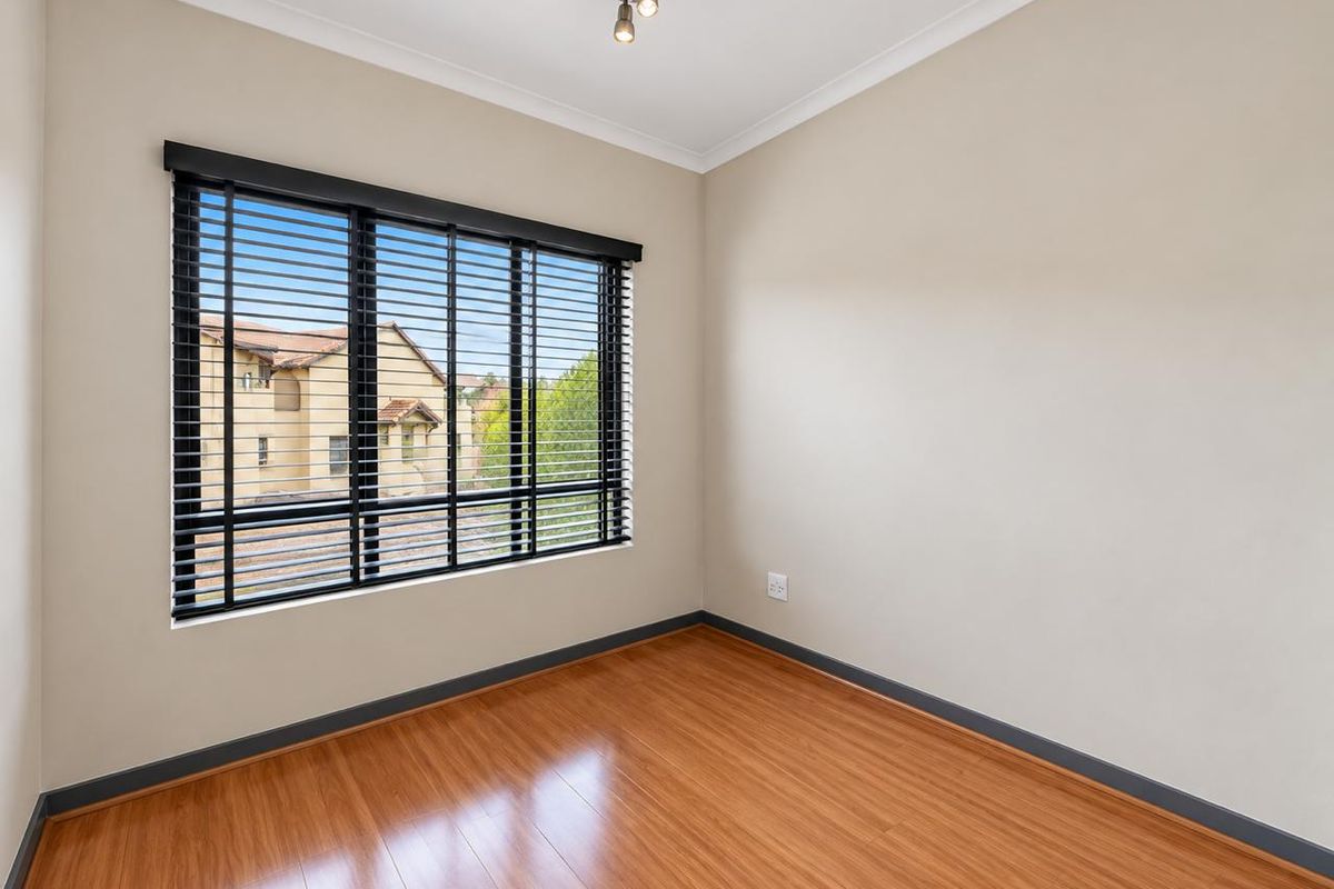 A bright, empty bedroom featuring laminate flooring, neutral walls, and black venetian blinds, offering a clean and versatile space ready for personalization.