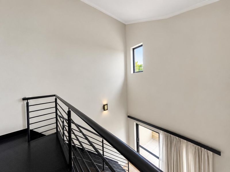 A bright, modern landing area featuring a sleek metal staircase with a matching balustrade, high ceilings, and natural light from a high-level window.