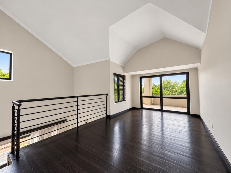 Spacious loft-style living area featuring high vaulted ceilings, dark hardwood flooring, a modern metal balustrade, and direct access to a private balcony.