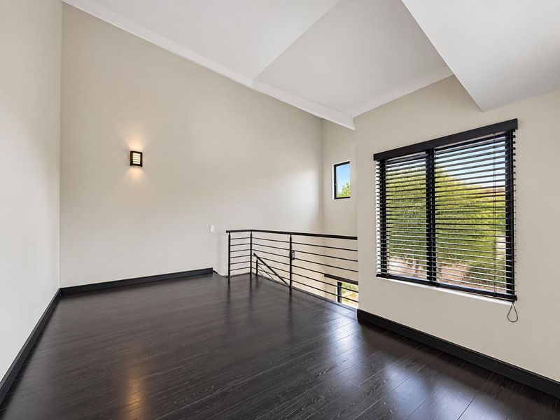 A bright, spacious landing or living area featuring dark timber flooring, a vaulted ceiling, and a modern metal balustrade overlooking the lower level.