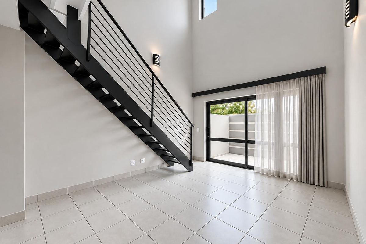 Spacious, modern living area featuring a striking black metal staircase, double-volume ceilings, tiled floors, and large sliding doors leading to an outdoor patio.