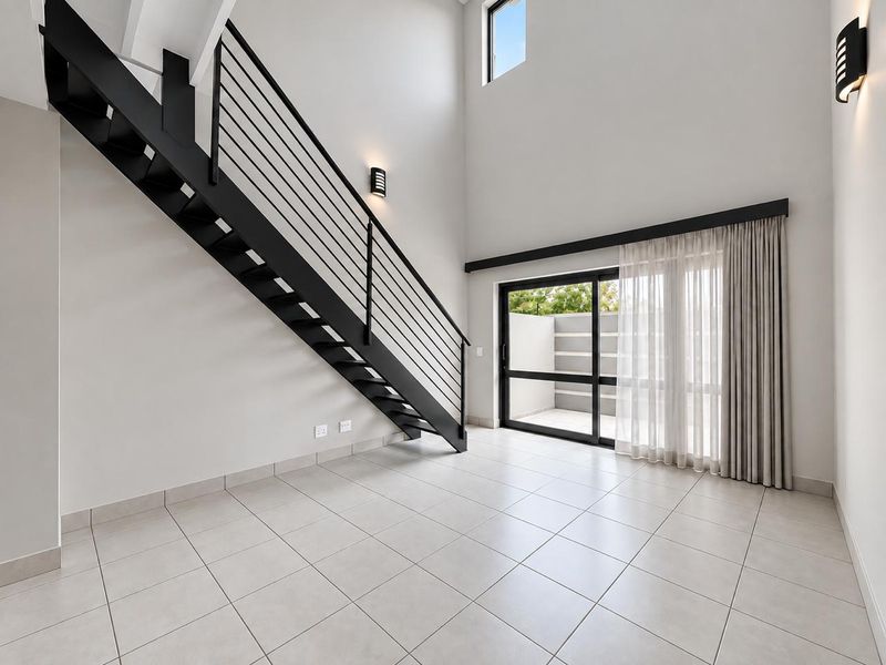 Spacious, modern living area featuring a striking black metal staircase, double-volume ceilings, tiled floors, and large sliding doors leading to an outdoor patio.