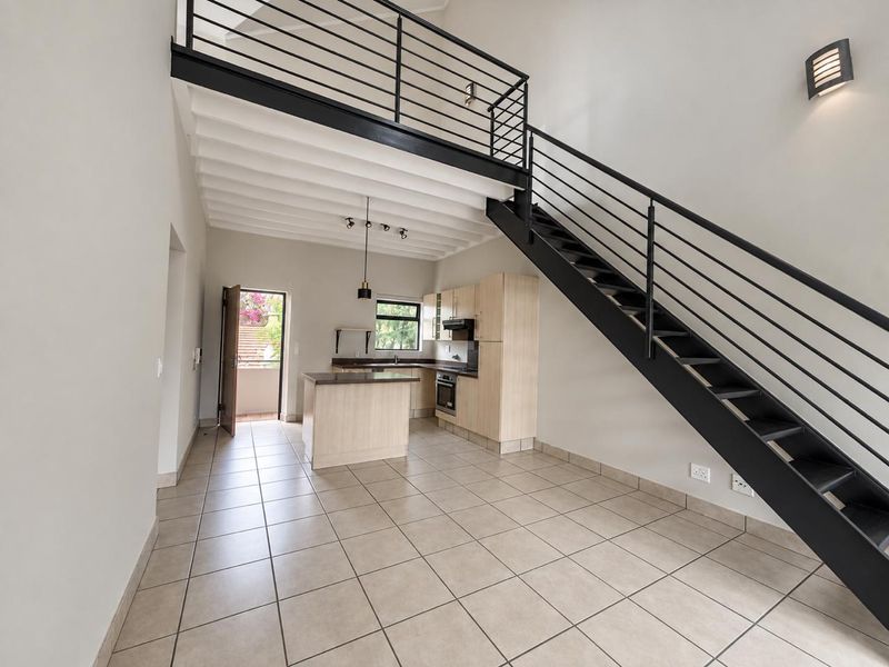 Open-plan kitchen and living area featuring tiled floors, modern cabinetry, and a striking metal staircase leading to a mezzanine level.