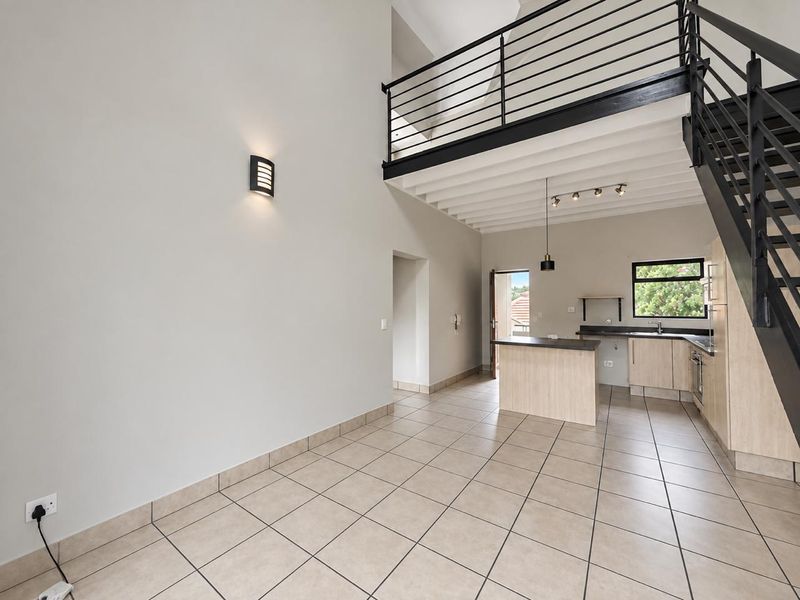 Spacious open-plan living and kitchen area featuring tiled floors, a modern staircase leading to a mezzanine level, and functional built-in cabinetry.