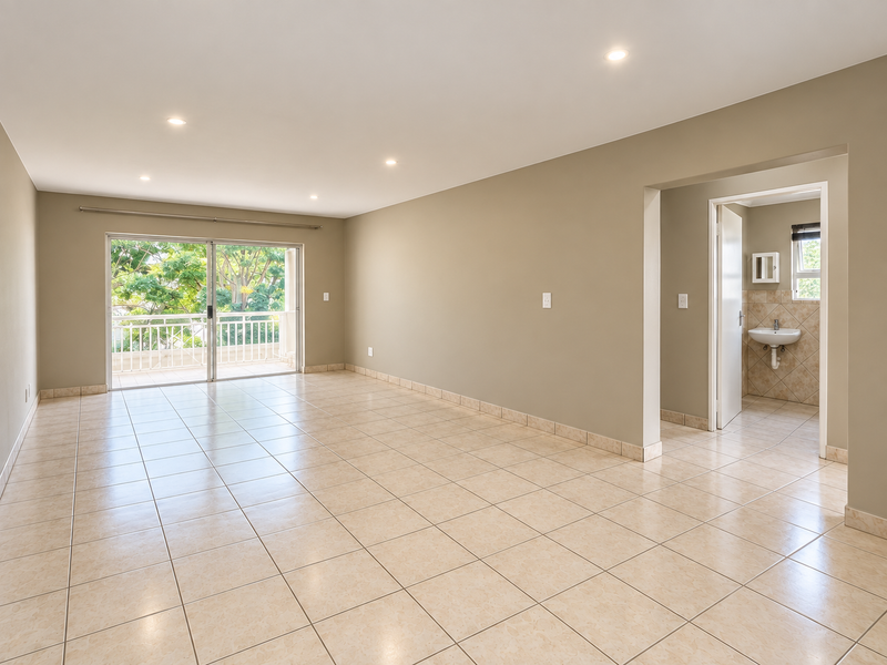 Spacious open-plan living area featuring neutral tiled flooring, recessed lighting, and a sliding door leading to a private balcony, with an adjacent bathroom.