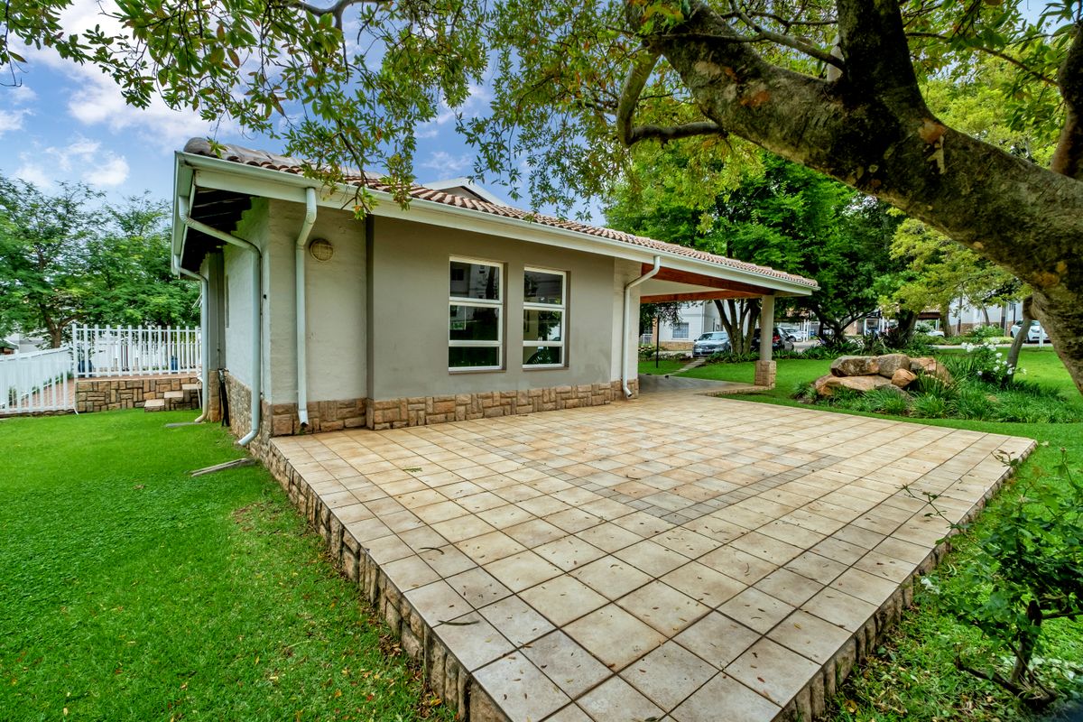 A well-maintained rear exterior view featuring a spacious tiled patio, stone cladding accents, and a covered veranda area set within a landscaped garden.
