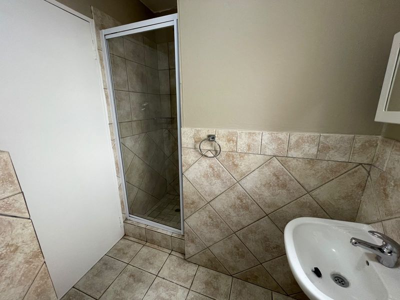 A functional bathroom featuring a shower enclosure with tiled surround, a pedestal basin with chrome mixer tap, and neutral floor tiling.