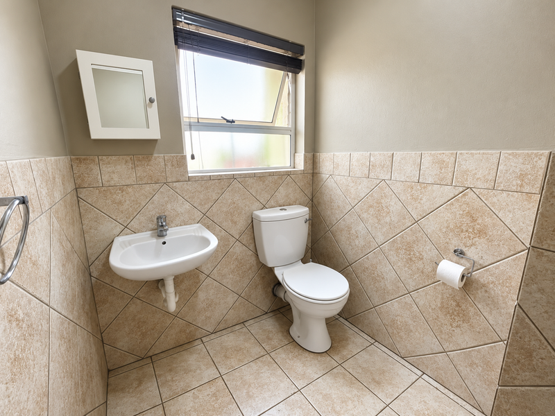 A clean and functional guest bathroom featuring neutral tiled walls, a wall-mounted basin, and a standard toilet with natural light from a top-hung window.