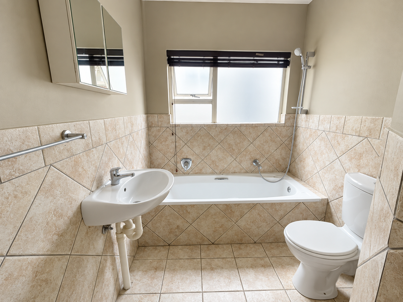 A functional bathroom featuring a bathtub with handheld shower mixer, wall-mounted basin, and toilet, finished with neutral wall tiles.