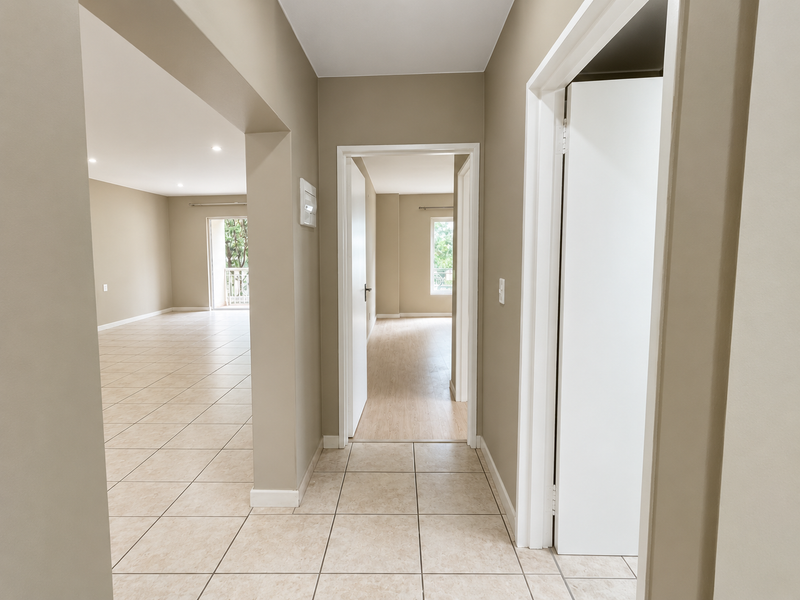 A bright, neutral-toned hallway connecting multiple living areas, featuring tiled flooring, clean white door frames, and recessed lighting throughout the apartment.