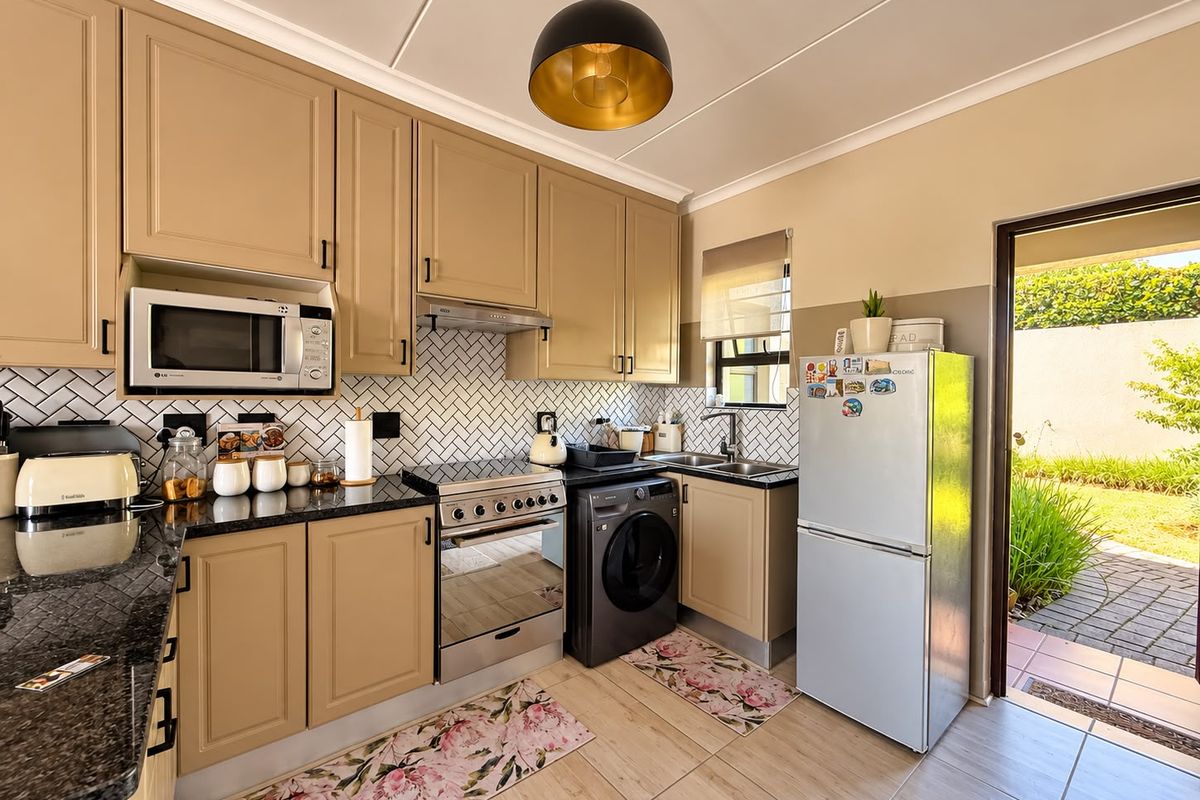 A well-maintained kitchen featuring neutral-toned cabinetry, granite countertops, a herringbone tile backsplash, and integrated appliances with direct access to an outdoor patio area.