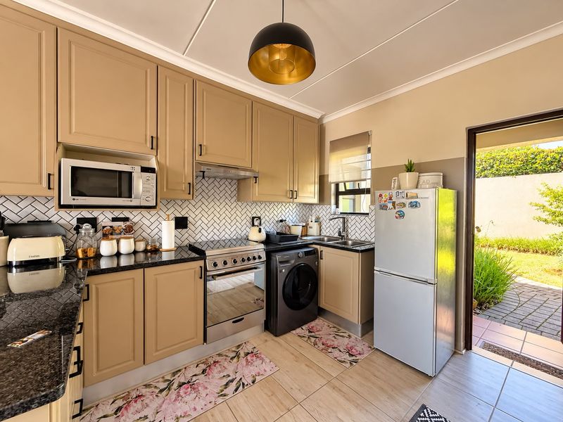 A well-maintained kitchen featuring neutral-toned cabinetry, granite countertops, a herringbone tile backsplash, and integrated appliances with direct access to an outdoor patio area.