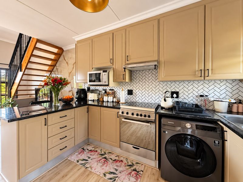A well-maintained kitchen featuring light-toned cabinetry, granite countertops, a stylish herringbone backsplash, and integrated appliances, adjacent to an open staircase.