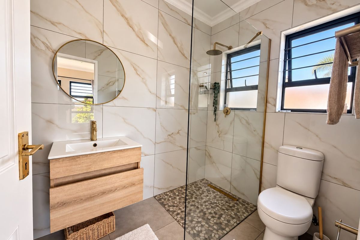 Modern bathroom featuring a floating vanity, brass fixtures, walk-in shower with pebble flooring, and elegant marble-look wall tiles.