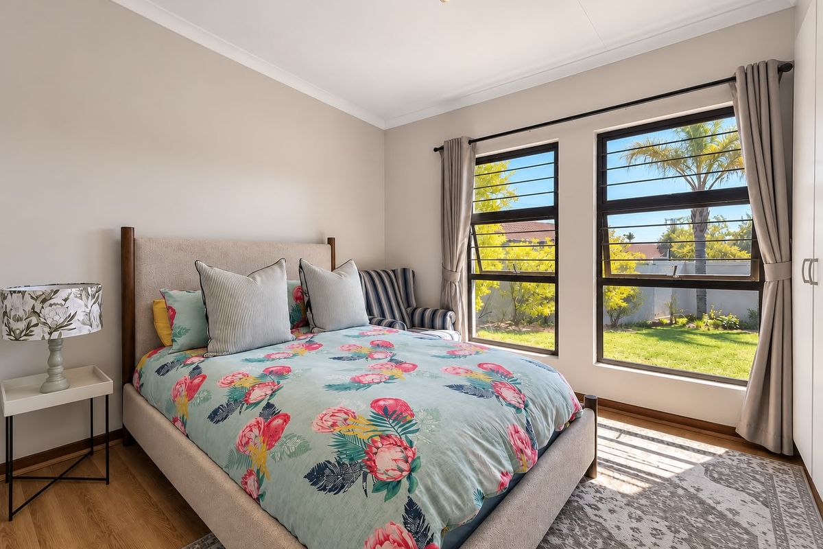 A well-maintained bedroom featuring laminate flooring, built-in cupboards, and large windows with security bars, offering a bright and comfortable living space.