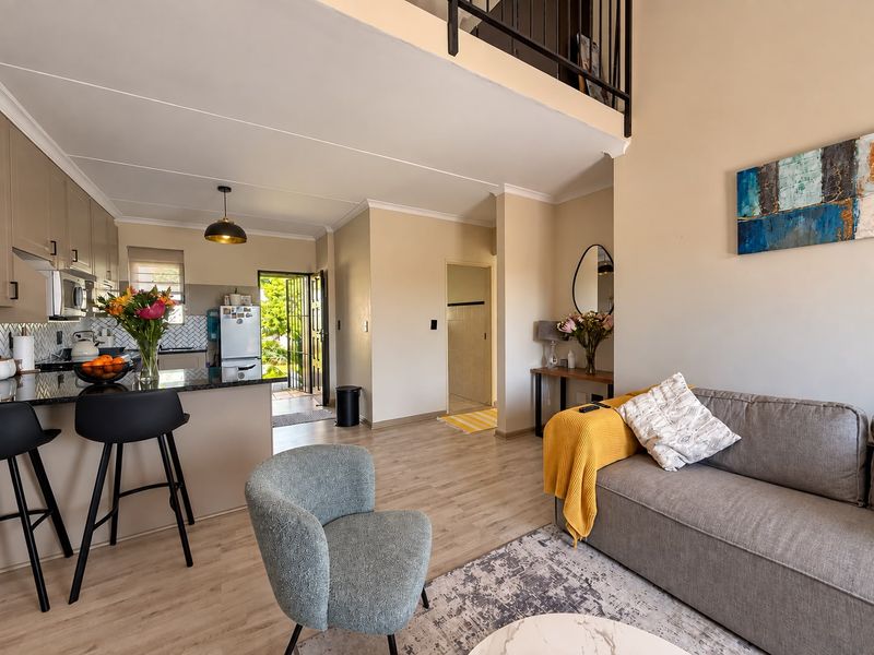 Open-plan living area featuring a modern kitchen with granite countertops, laminate flooring, and a mezzanine level with a metal staircase railing.