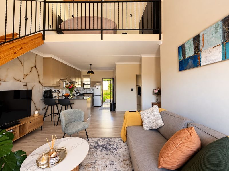 A bright open-plan living area featuring a modern kitchen, marble-effect feature wall, and a mezzanine level with a wrought iron balustrade.