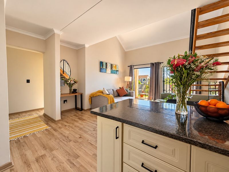 Bright open-plan living area featuring a modern kitchen with granite countertops, laminate flooring, and a wooden staircase leading to the upper level.