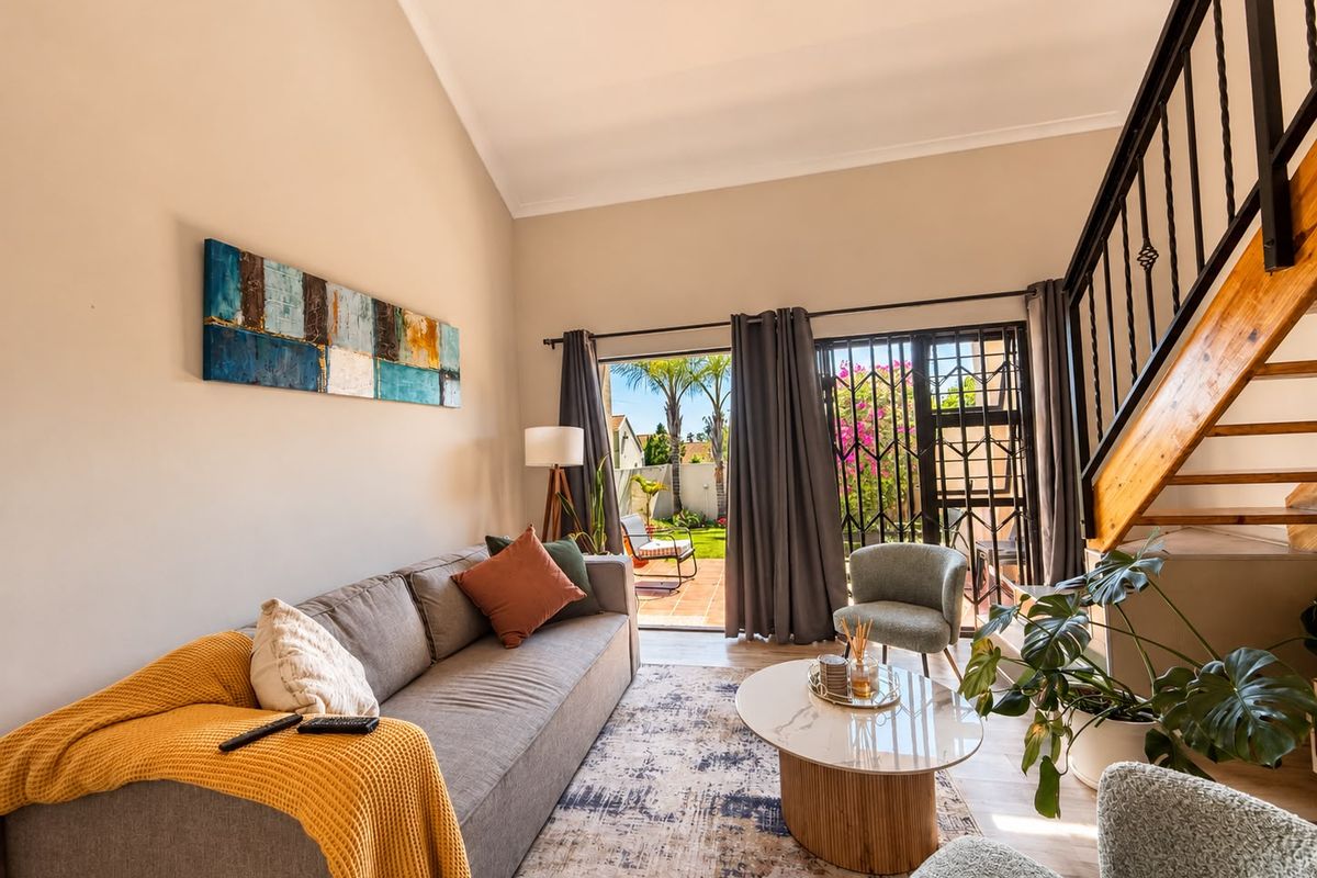 A bright living room featuring a vaulted ceiling, staircase with metal balustrades, and direct access to the rear garden through a sliding glass door.