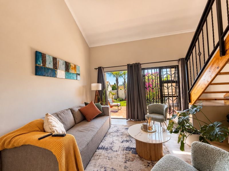 A bright living room featuring a vaulted ceiling, staircase with metal balustrades, and direct access to the rear garden through a sliding glass door.