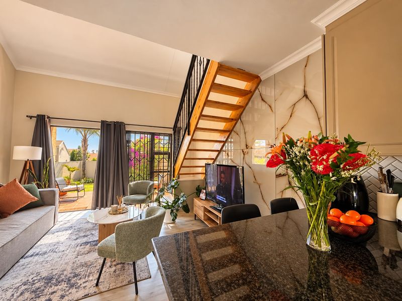 Modern open-plan living area featuring a sleek wooden staircase, marble-look feature wall, granite kitchen island, and seamless access to a private patio.