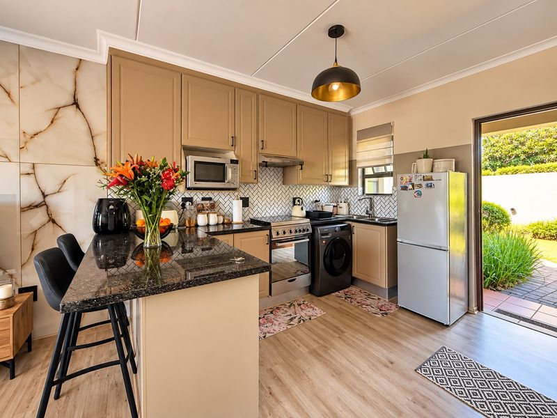Modern kitchen featuring granite countertops, herringbone backsplash, built-in cabinetry, and integrated appliances, with direct access to the rear garden area.