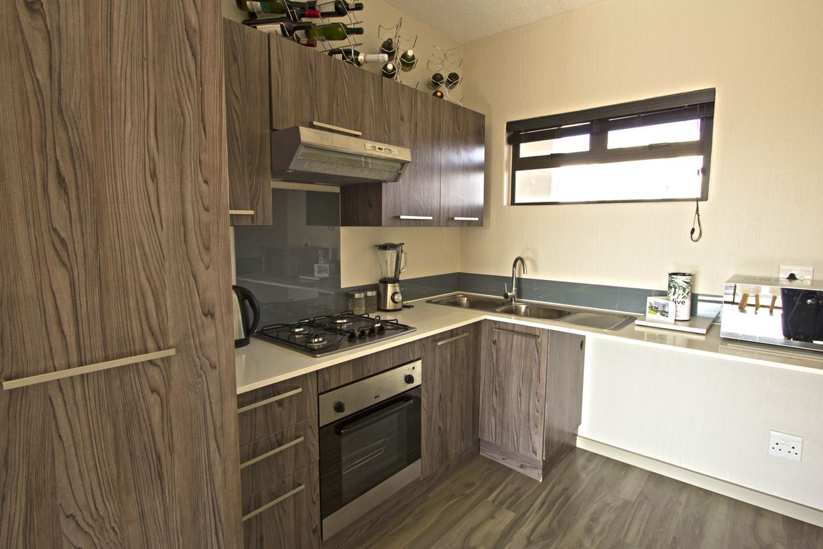 Modern kitchen featuring wood-grain laminate cabinetry, stone countertops, a gas hob with extractor, and a stainless steel double sink.