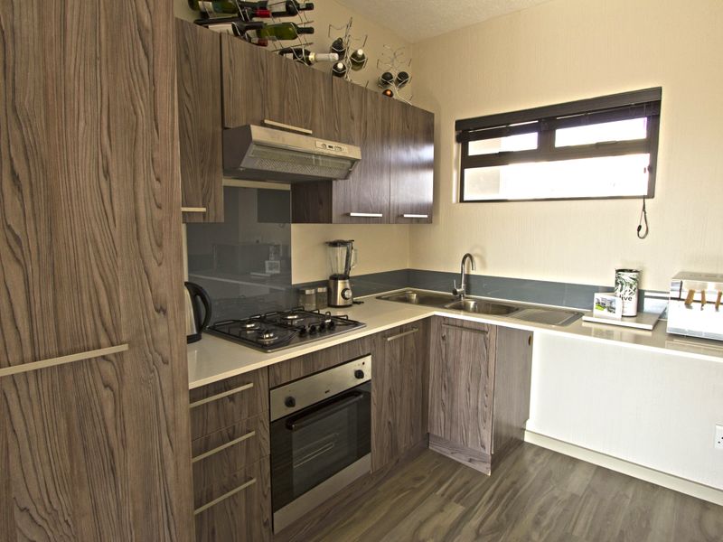 Modern kitchen featuring wood-grain laminate cabinetry, stone countertops, a gas hob with extractor, and a stainless steel double sink.