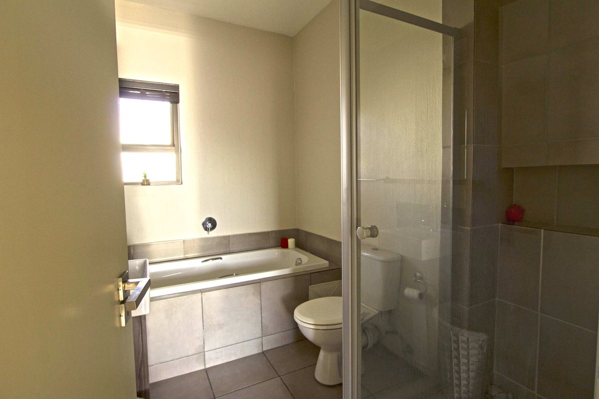 A functional bathroom featuring a built-in bathtub, a separate glass-enclosed shower, and neutral tiled finishes throughout.