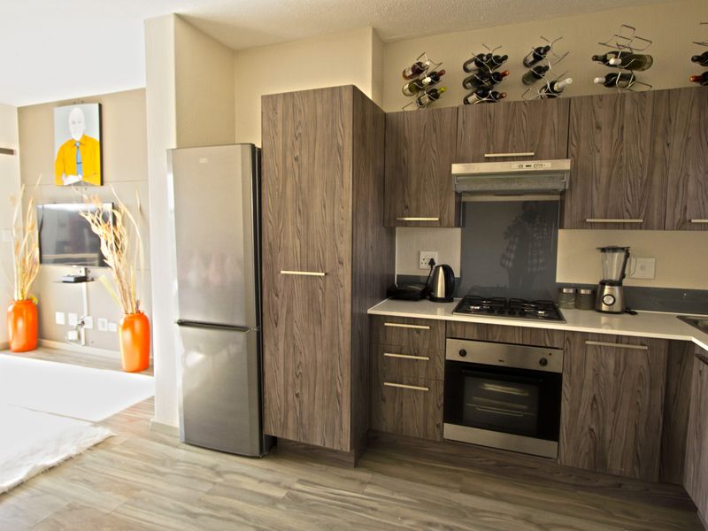 Modern open-plan kitchen featuring wood-grain cabinetry, stone countertops, and integrated appliances, seamlessly flowing into the adjacent living area.