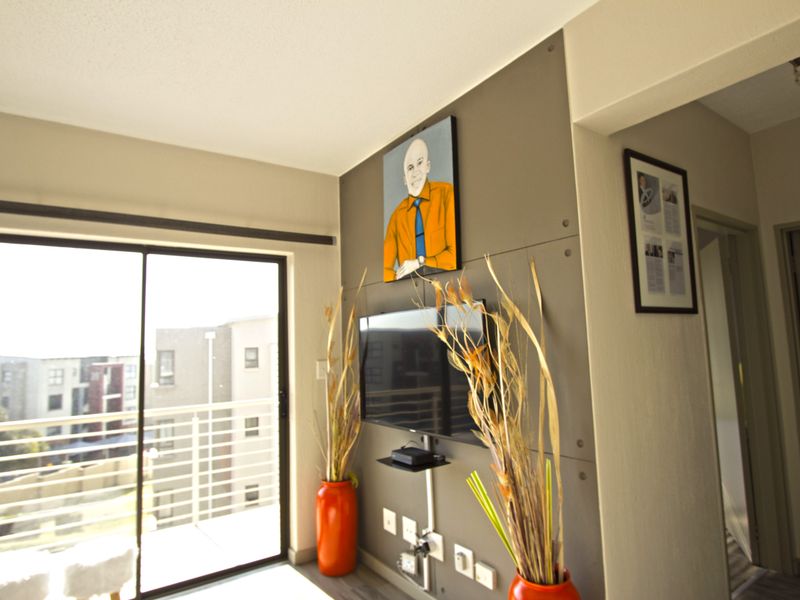 A living room featuring a modern accent wall with a mounted television and large sliding glass doors providing access to a balcony.