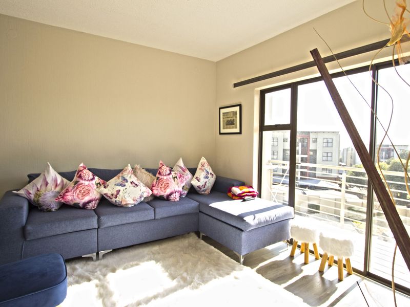 A bright living room featuring laminate flooring and a large sliding glass door that opens onto a balcony with urban views.