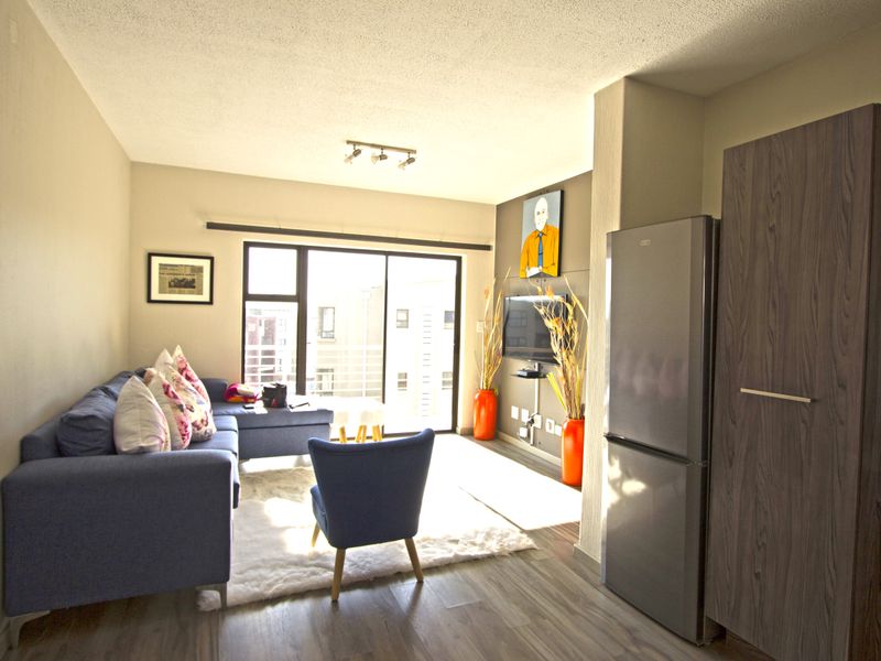An open-plan living area featuring modern laminate flooring, neutral walls, and a sliding glass door leading to a balcony.