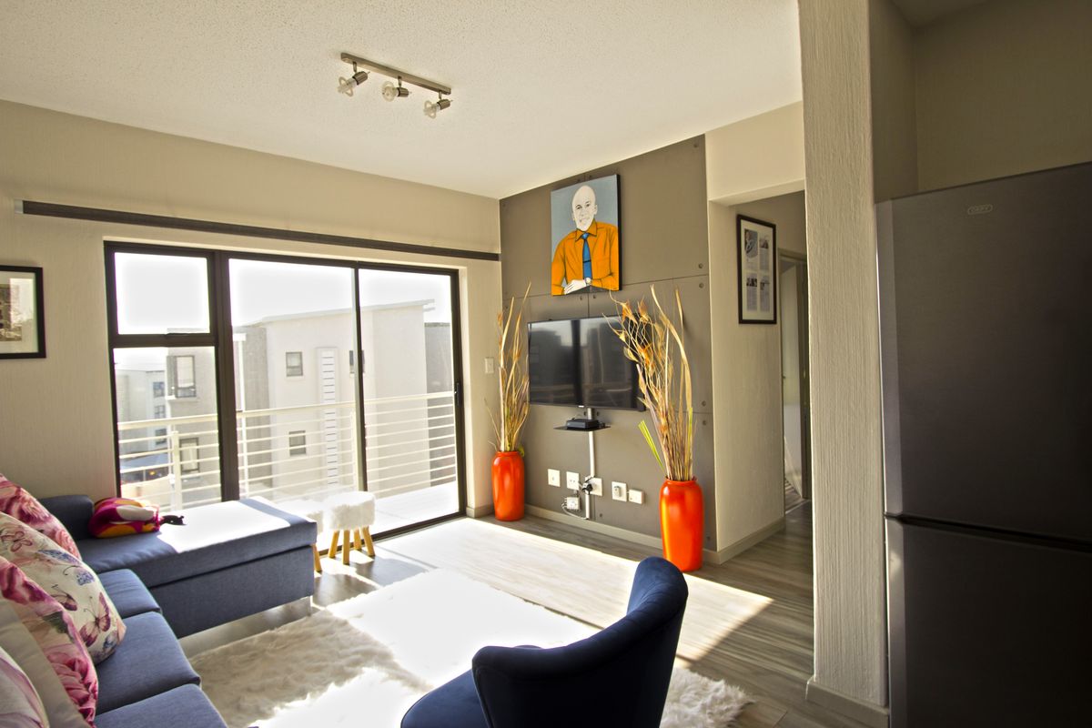 A bright living room featuring laminate flooring, a modern accent wall, and large sliding glass doors that open onto a balcony.