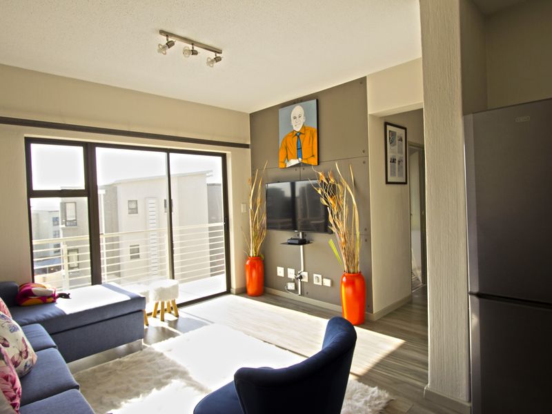 A bright living room featuring laminate flooring, a modern accent wall, and large sliding glass doors that open onto a balcony.
