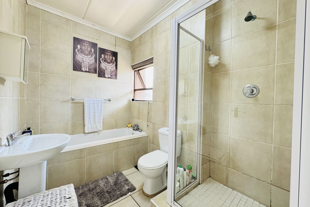 A functional bathroom featuring a pedestal basin, built-in bathtub, and a separate shower enclosure with tiled finishes throughout.