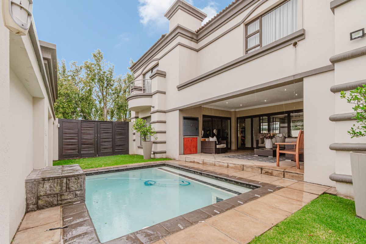 Rear exterior view featuring a swimming pool, covered patio area with built-in braai, and a well-maintained garden space.