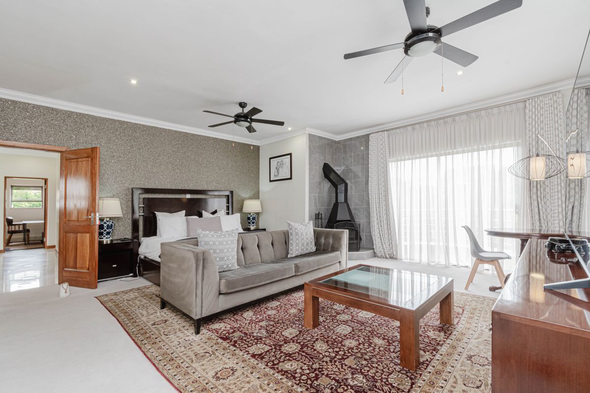 Spacious bedroom featuring a cozy seating area, a freestanding fireplace, ceiling fans, and large sliding glass doors that provide ample natural light.