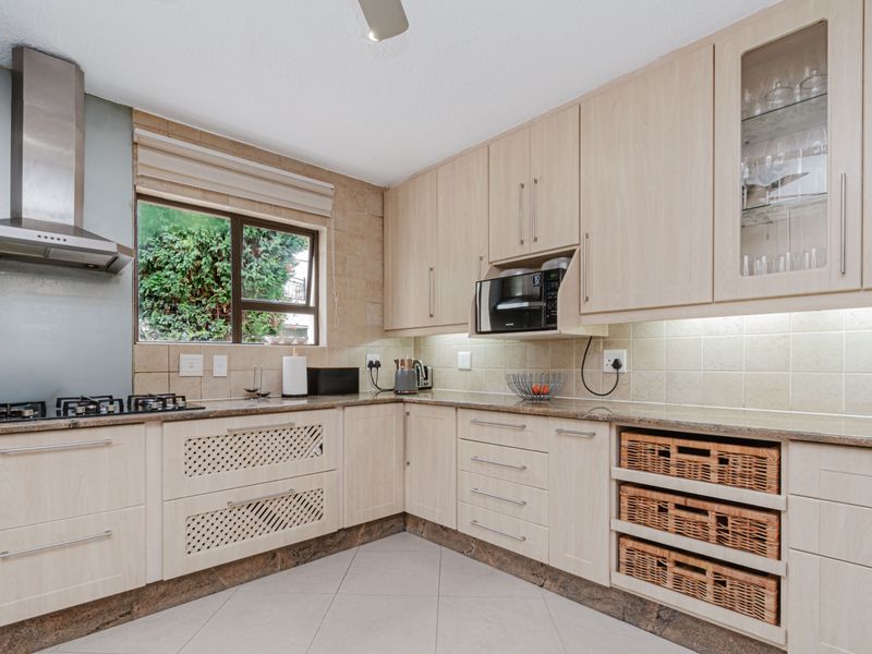 A well-maintained kitchen featuring light wood cabinetry, granite countertops, a gas hob with stainless steel extractor, and integrated storage solutions.