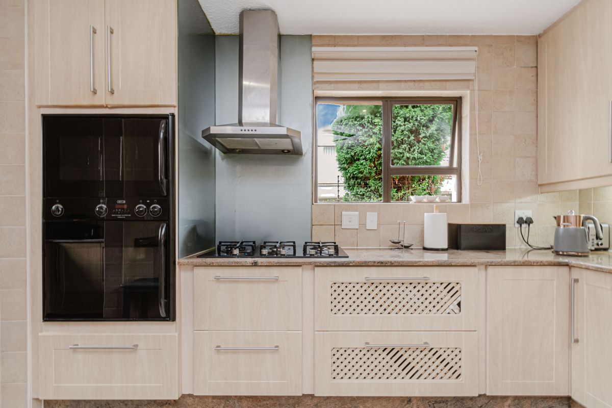 A well-maintained kitchen featuring light wood cabinetry, granite countertops, a built-in oven, gas hob, and a stainless steel extractor fan.