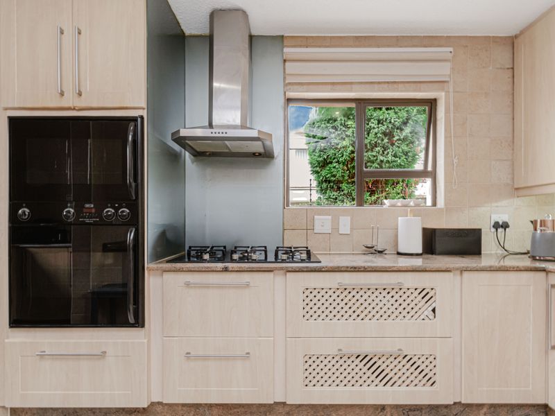 A well-maintained kitchen featuring light wood cabinetry, granite countertops, a built-in oven, gas hob, and a stainless steel extractor fan.