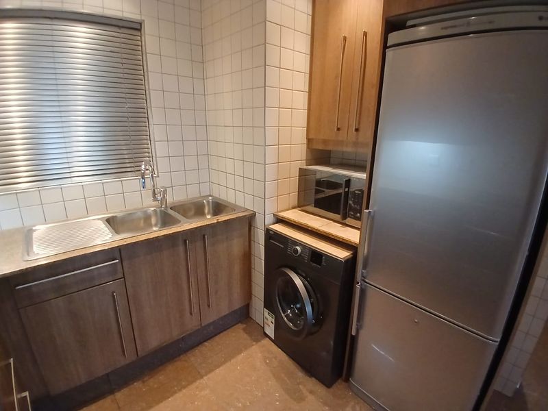 Functional laundry area featuring built-in cabinetry, a double stainless steel sink, tiled splashback, and space for integrated appliances.