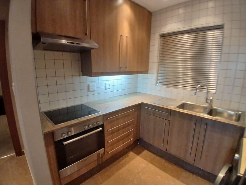 A functional kitchen featuring wood-finish cabinetry, integrated stainless steel appliances, a tiled backsplash, and a double sink with a window view.