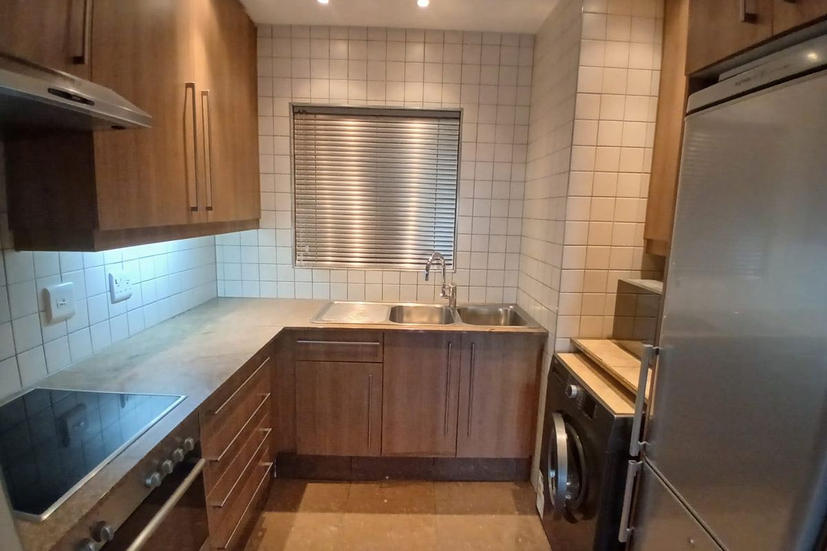 Compact kitchen featuring wood-finish cabinetry, tiled backsplash, integrated oven and hob, and a stainless steel sink with a window view.